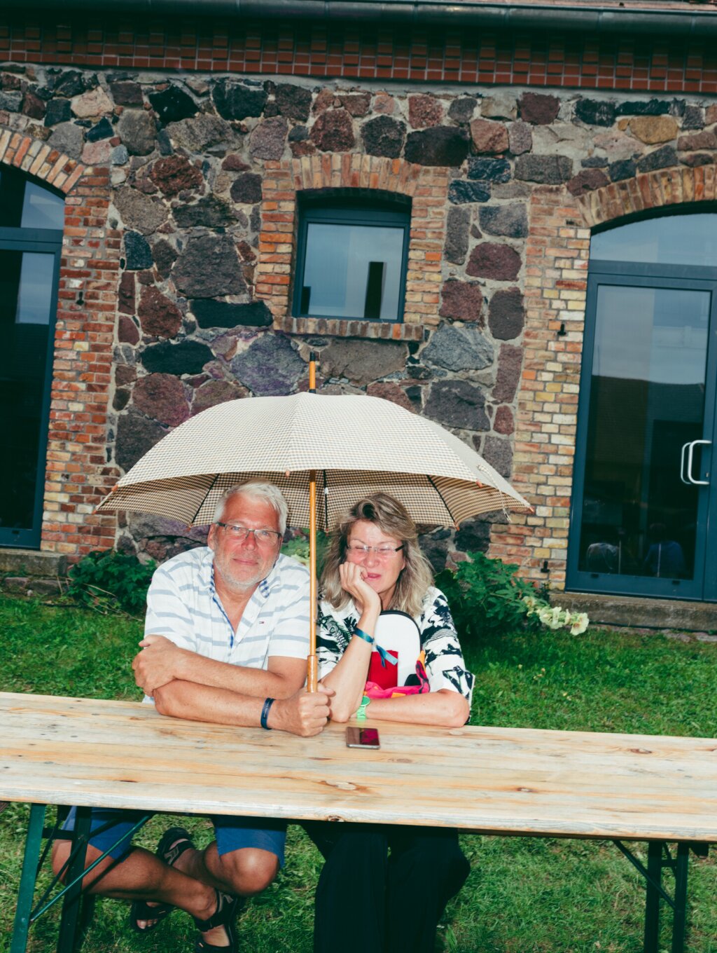 A couple is sitting under an umbrella at a beer table, the woman is smiling.